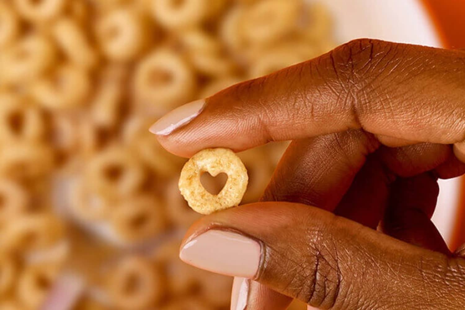 A hand holding a single Cheerio with a heart center in focus